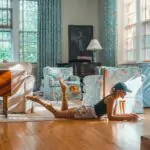woman lying on brown floor near blue and white sofa set inside white room with glass windows at daytime